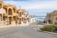 an empty street with a car driving through it near the ocean area and houses on the left side