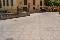 a large brick area has several benches and tables with people sitting in the background on a sunny day