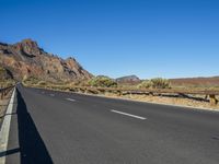 a long straight road in front of mountains and dry grass area under blue sky with no clouds