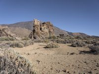 a rocky landscape with a desert field and mountain in the background, and a clear blue sky