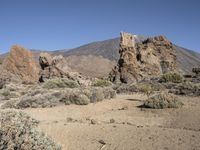 a rocky landscape with a desert field and mountain in the background, and a clear blue sky