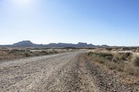 an empty road in a wide open plain of land near mountains and water on a sunny day