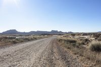 an empty road in a wide open plain of land near mountains and water on a sunny day