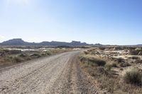 an empty road in a wide open plain of land near mountains and water on a sunny day