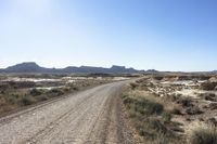 an empty road in a wide open plain of land near mountains and water on a sunny day