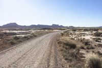 an empty road in a wide open plain of land near mountains and water on a sunny day