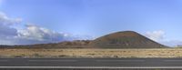 road passing through barren desert land in front of a mountain range with a blue sky