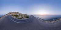 a curved road going to the ocean in front of a mountain top at dusk over the ocean