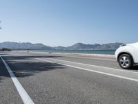 car moving along a paved highway near the ocean with mountains in background on a sunny day