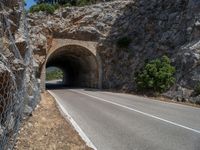 a road through the stone tunnel in a mountainous area is shown on a sunny day