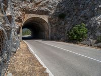 a road through the stone tunnel in a mountainous area is shown on a sunny day