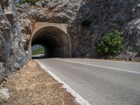 a road through the stone tunnel in a mountainous area is shown on a sunny day