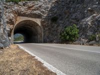 a road through the stone tunnel in a mountainous area is shown on a sunny day