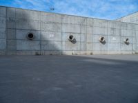 the empty parking lot in front of a wall with apartment buildings on it and a skateboarder on a ramp