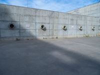 the empty parking lot in front of a wall with apartment buildings on it and a skateboarder on a ramp