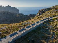 a long concrete road leads to the ocean in the distance with mountains and grassy land