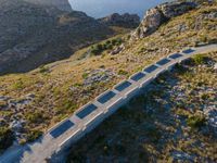 a long concrete road leads to the ocean in the distance with mountains and grassy land