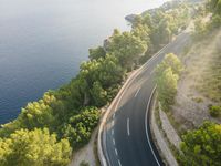 an aerial view of a highway leading along a cliff by the ocean on a sunny day