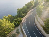 an aerial view of a highway leading along a cliff by the ocean on a sunny day