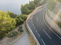 an aerial view of a highway leading along a cliff by the ocean on a sunny day