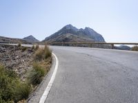 a motorcyclist is riding on the side of the road with a mountain in the background