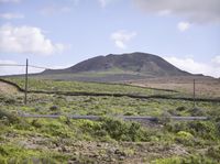 a hill with a telephone tower in the background and a road running between it on a grassy plain