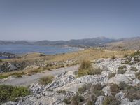 the hills are barren and filled with grass and shrubs on top of the rocks is the ocean