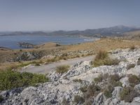 the hills are barren and filled with grass and shrubs on top of the rocks is the ocean