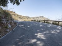 a scenic road curves along side a hillside and a hill, looking up at the sky