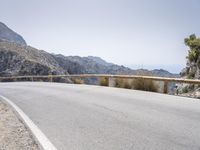 a lone motor bike is parked along an empty road near the ocean, in the distance are mountains