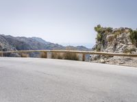 a lone motor bike is parked along an empty road near the ocean, in the distance are mountains