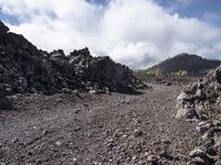 a dirt field with boulders and boulders in it and sky and clouds in the background