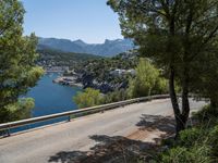 an empty road winding down the side of a body of water near the mountains and a village