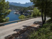 an empty road winding down the side of a body of water near the mountains and a village