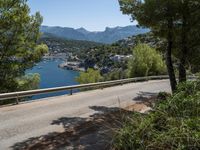 an empty road winding down the side of a body of water near the mountains and a village