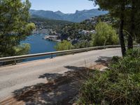 an empty road winding down the side of a body of water near the mountains and a village