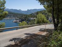 an empty road winding down the side of a body of water near the mountains and a village