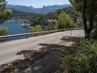 an empty road winding down the side of a body of water near the mountains and a village