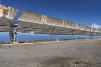 large solar array sitting on top of dirt field next to water and a street light