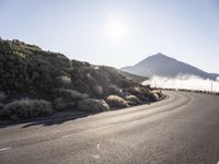 an empty empty road in front of the sun and mountains with a fog on it