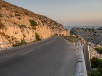 a winding road on a cliff overlooking a sea and a lighthouse tower at sunset, a view from behind