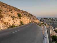 a winding road on a cliff overlooking a sea and a lighthouse tower at sunset, a view from behind