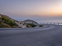 winding asphalt roadway near sea and cliffs on the horizon with sunset in the sky above