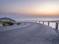 winding asphalt roadway near sea and cliffs on the horizon with sunset in the sky above