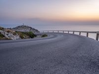 winding asphalt roadway near sea and cliffs on the horizon with sunset in the sky above