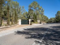 a paved road with a gate and several bushes near the side of it near a park