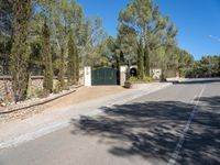 a paved road with a gate and several bushes near the side of it near a park