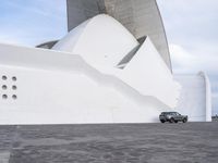 a car is parked in front of a building with curved concrete roofs and doors and a circular roof