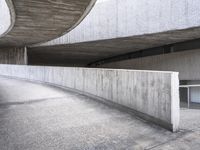 the long curved wall of a cement building next to a metal staircase with a railing