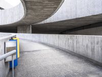 the long curved wall of a cement building next to a metal staircase with a railing